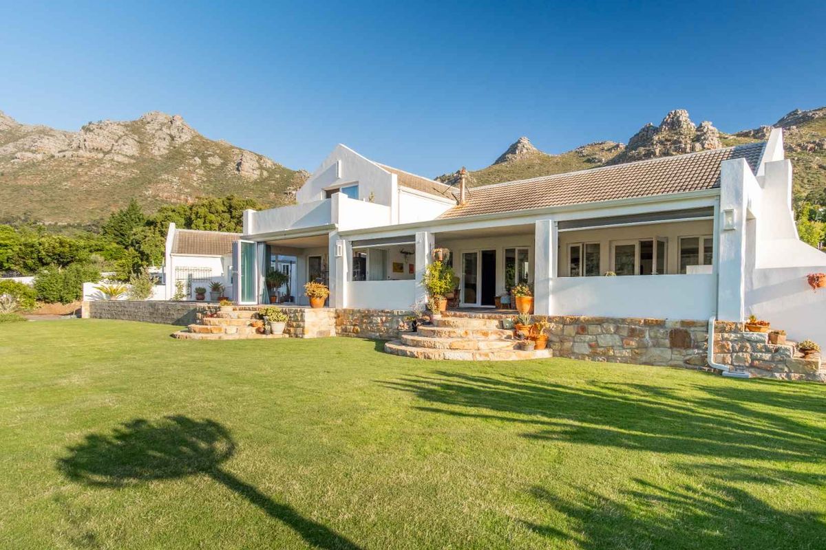 A beautiful rear elevation of a white house featuring stone-clad foundations, a spacious covered patio, and expansive lawn with mountain views.
