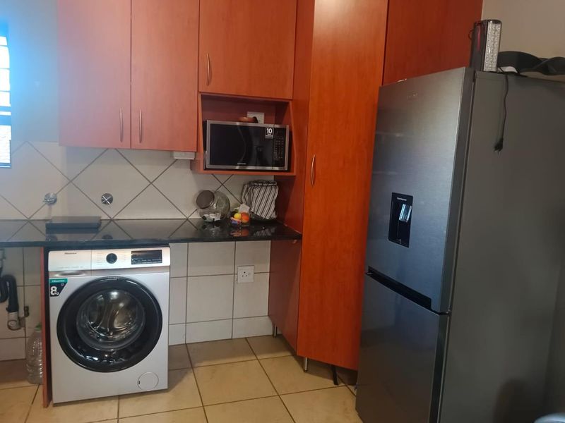A functional kitchen area featuring wood-finish cabinetry, granite countertops, tiled backsplash, and dedicated space for laundry appliances.