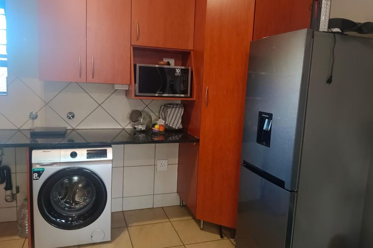 A functional kitchen area featuring wood-finish cabinetry, granite countertops, tiled backsplash, and dedicated space for laundry appliances.