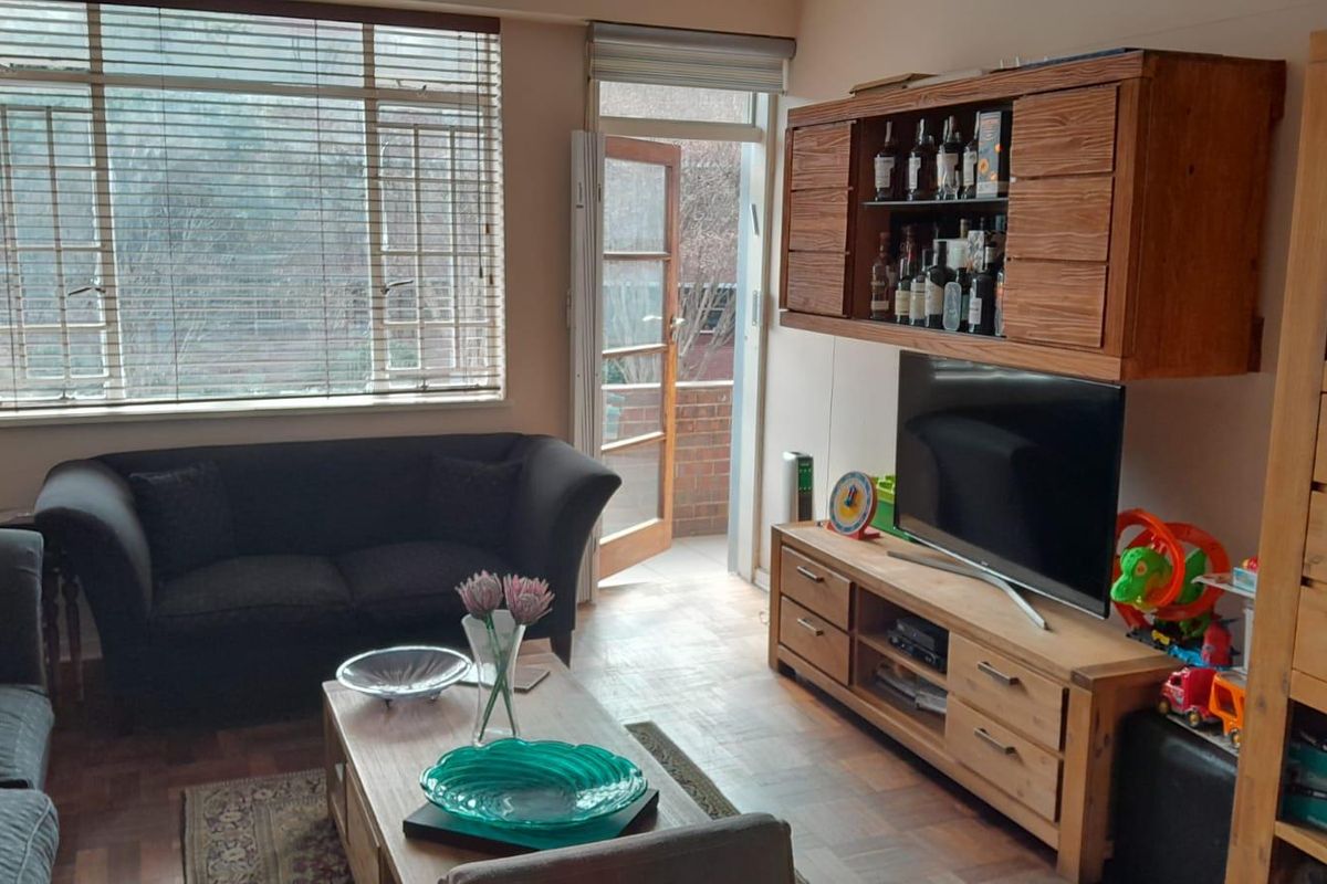 A living room featuring parquet flooring, large windows with venetian blinds, and direct access to an outdoor balcony area.
