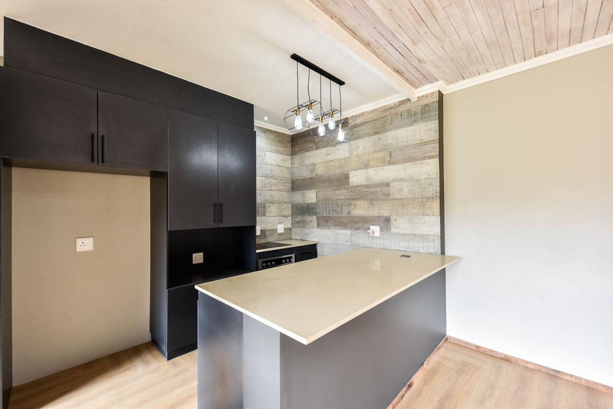 Modern kitchen featuring a breakfast bar, built-in cabinetry, integrated cooktop, and stylish wood-paneled accent wall with contemporary pendant lighting.