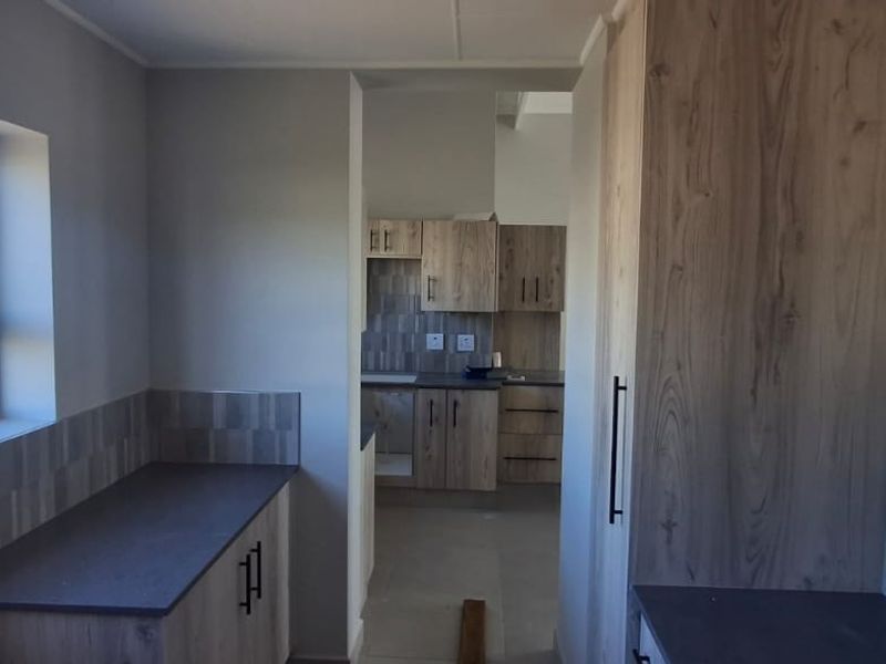 A modern, empty kitchen featuring wood-look cabinetry, dark laminate countertops, and tiled backsplashes, offering a clean and functional layout.
