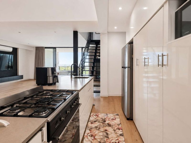 Modern open-plan kitchen and living area featuring high-gloss cabinetry, a gas hob, kitchen island, and a staircase leading to the upper level.