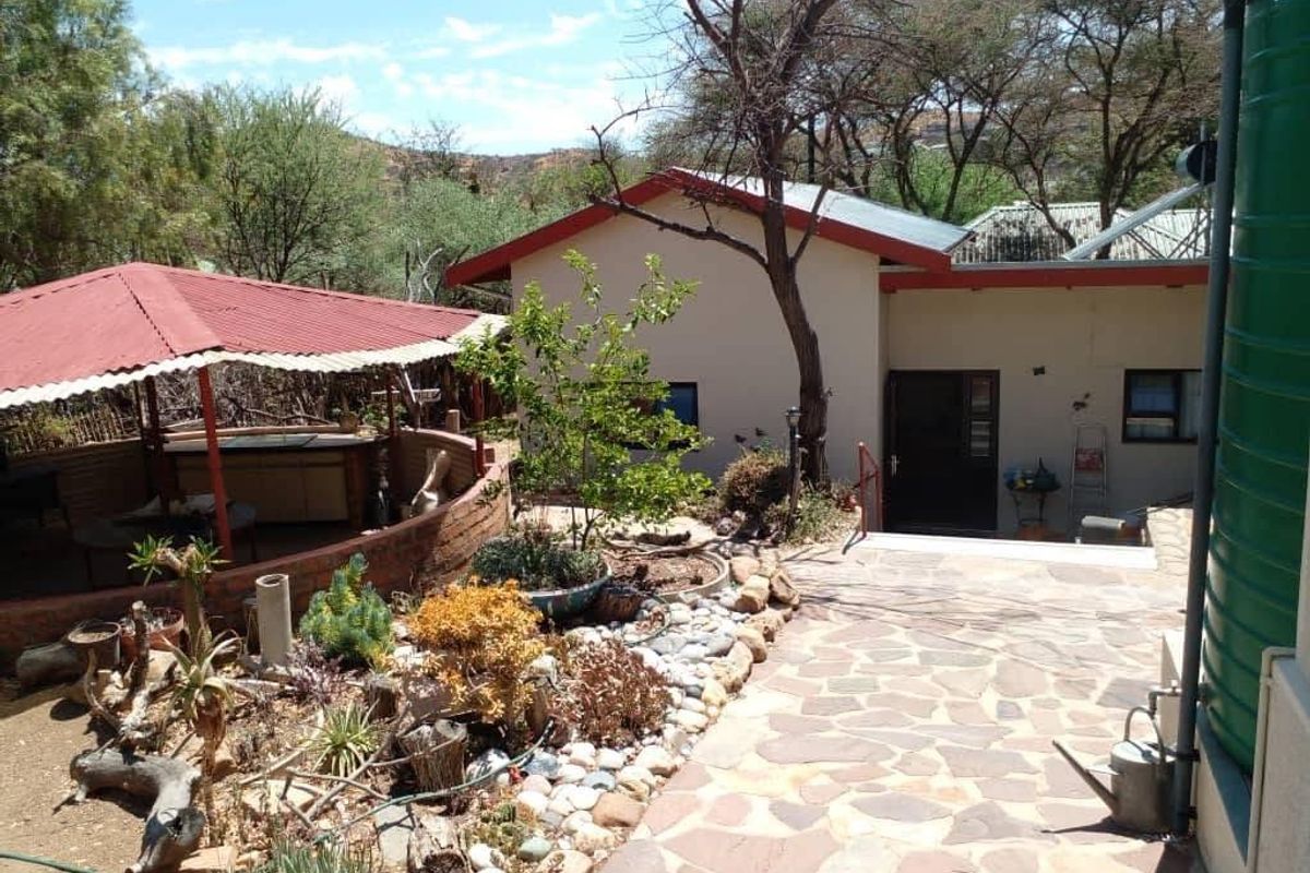 Rear exterior view featuring a stone paved walkway, a covered patio area with a brick retaining wall, and a large water storage tank.