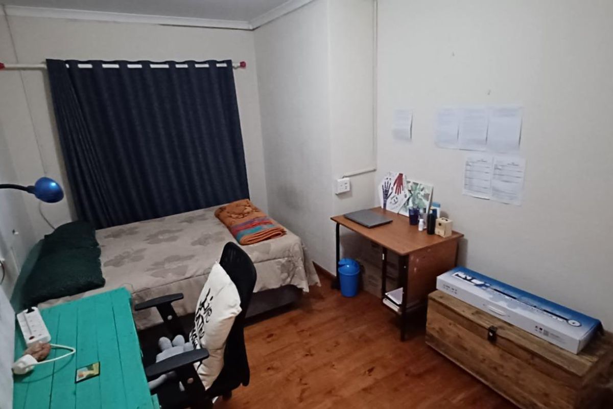 A functional bedroom featuring timber-look flooring, a window with curtain track, and standard electrical outlets.
