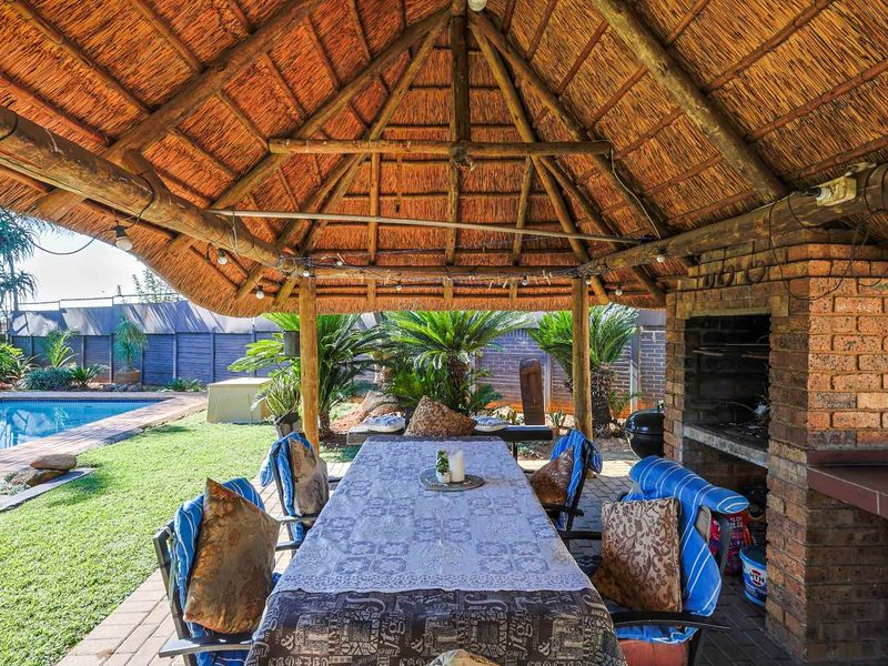 Covered outdoor entertainment area featuring a traditional thatched roof, built-in brick braai, and direct access to the swimming pool and garden.