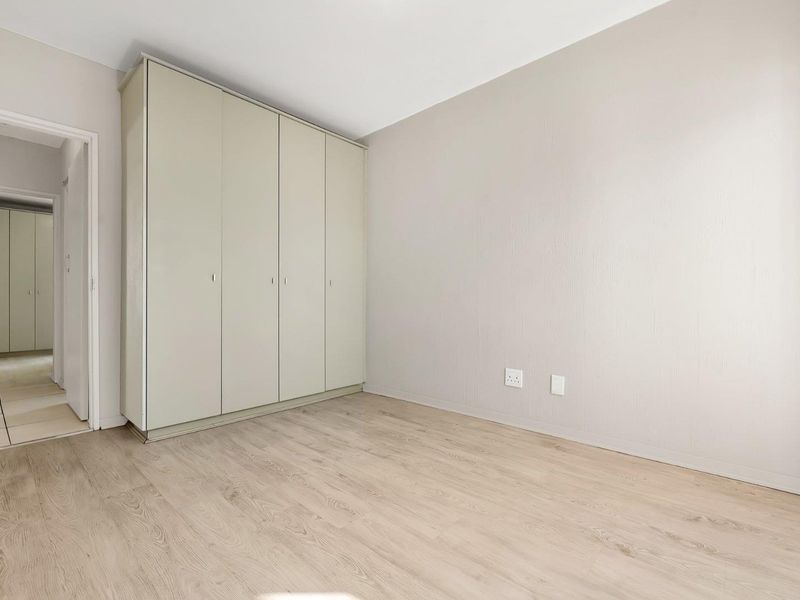 A bright, empty bedroom featuring neutral walls, light-toned laminate flooring, and built-in cupboards, offering a clean and versatile space.