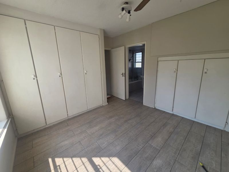 A spacious, empty bedroom featuring extensive built-in cupboard storage, modern wood-look tile flooring, and direct access to an adjoining bathroom.