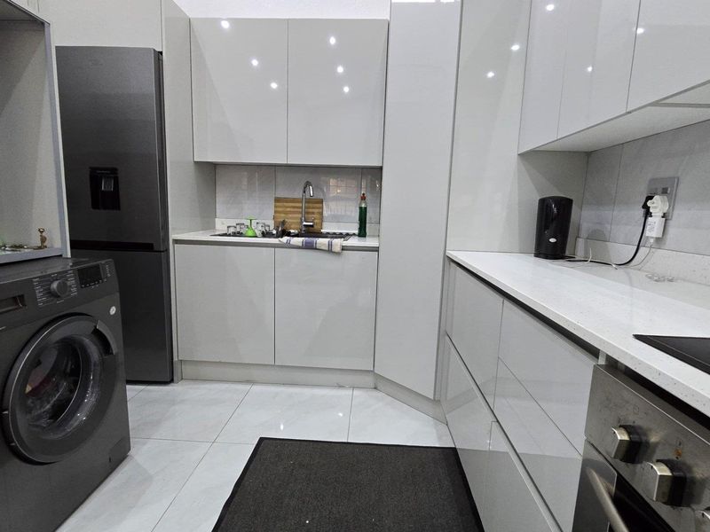 Modern kitchen featuring high-gloss cabinetry, stone countertops, integrated oven and cooktop, and sleek tiled flooring in a contemporary townhouse setting.