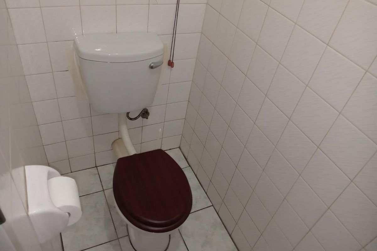 A compact bathroom featuring a standard white toilet with a dark wood-effect seat and fully tiled wall and floor surfaces.