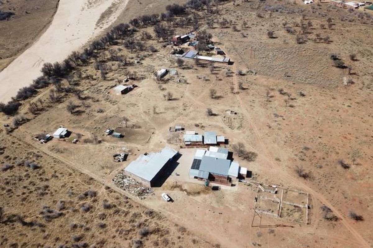Aerial view of a rural small holding featuring multiple outbuildings, metal roof structures, solar panels, and fenced enclosures set within a large landscape.