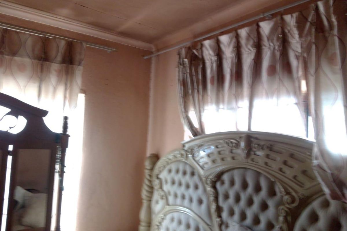 A bedroom interior featuring a corner view with visible ceiling cracks and dated wall finishes.