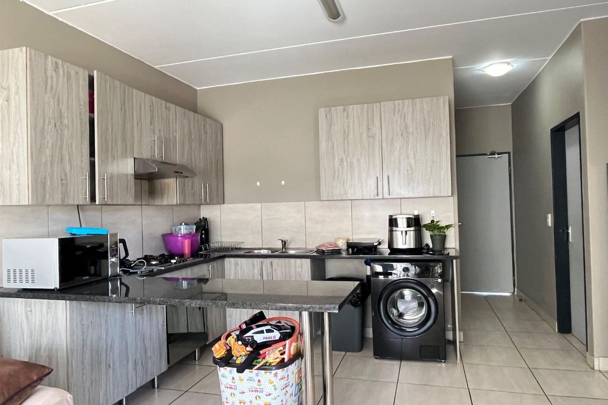 Functional kitchen featuring light wood-grain cabinetry, granite countertops, a gas hob with extractor, and integrated laundry plumbing, finished with neutral floor tiles.