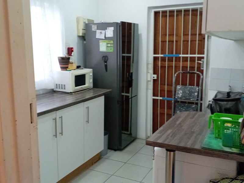 A functional kitchen area featuring white cabinetry, laminate countertops, and tiled flooring, with a security gate leading to the exterior.