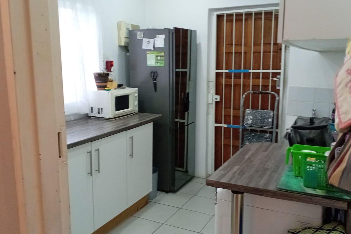 A functional kitchen area featuring white cabinetry, laminate countertops, and tiled flooring, with a security gate leading to the exterior.