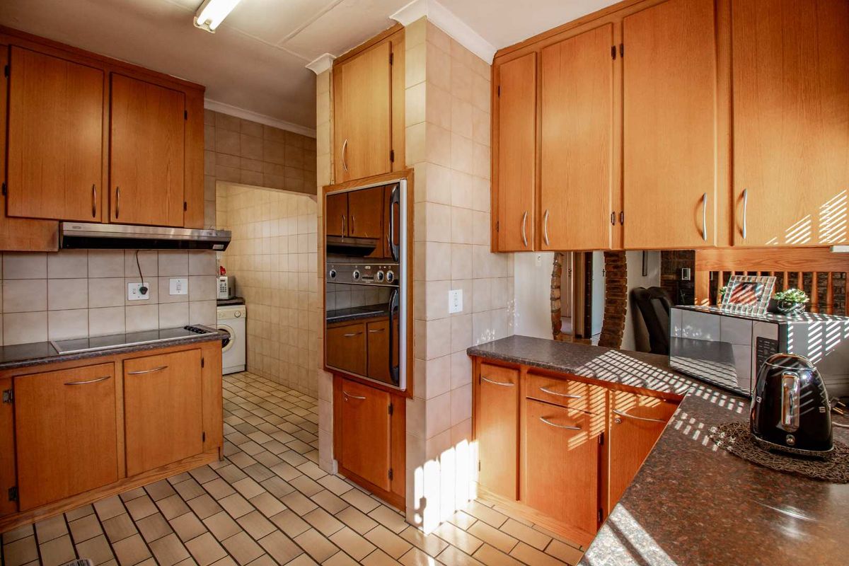 A functional kitchen featuring wood-finish cabinetry, built-in oven, integrated hob, and tiled flooring, with an adjacent scullery area.