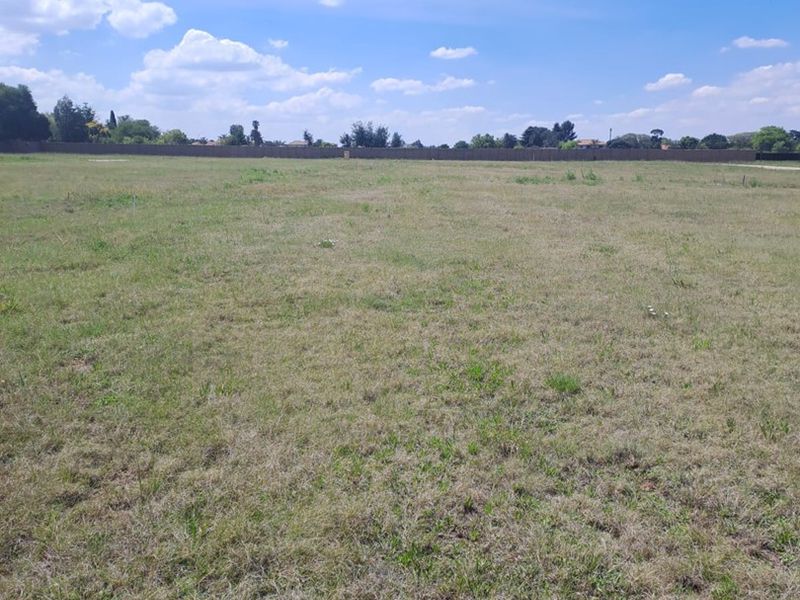 A wide, open vacant residential plot featuring level grass terrain and perimeter boundary fencing.