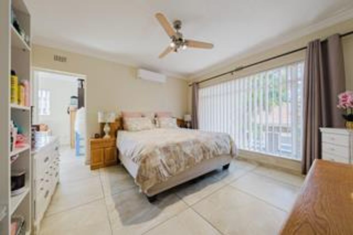 Spacious bedroom featuring tiled flooring, a ceiling fan, and a wall-mounted split-system air conditioner, with large windows providing natural light.