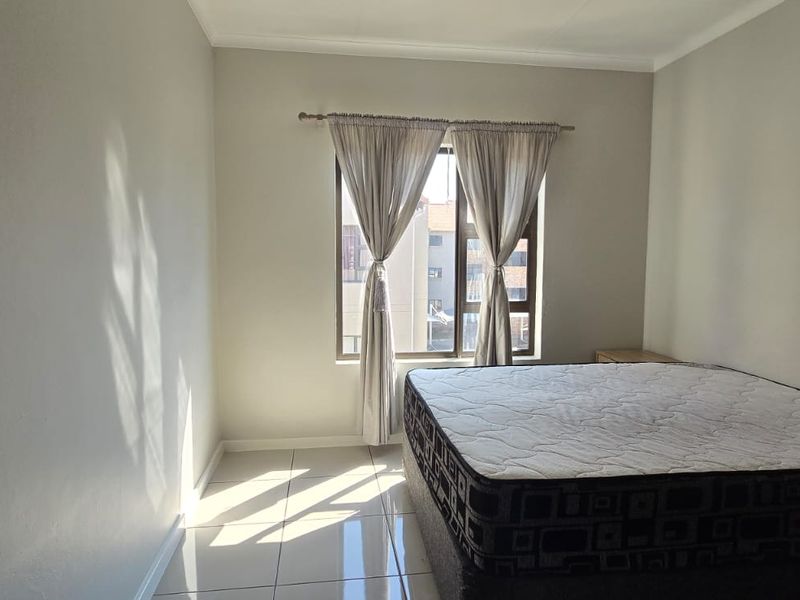 A simple bedroom featuring tiled flooring and a window that allows natural light into the space.