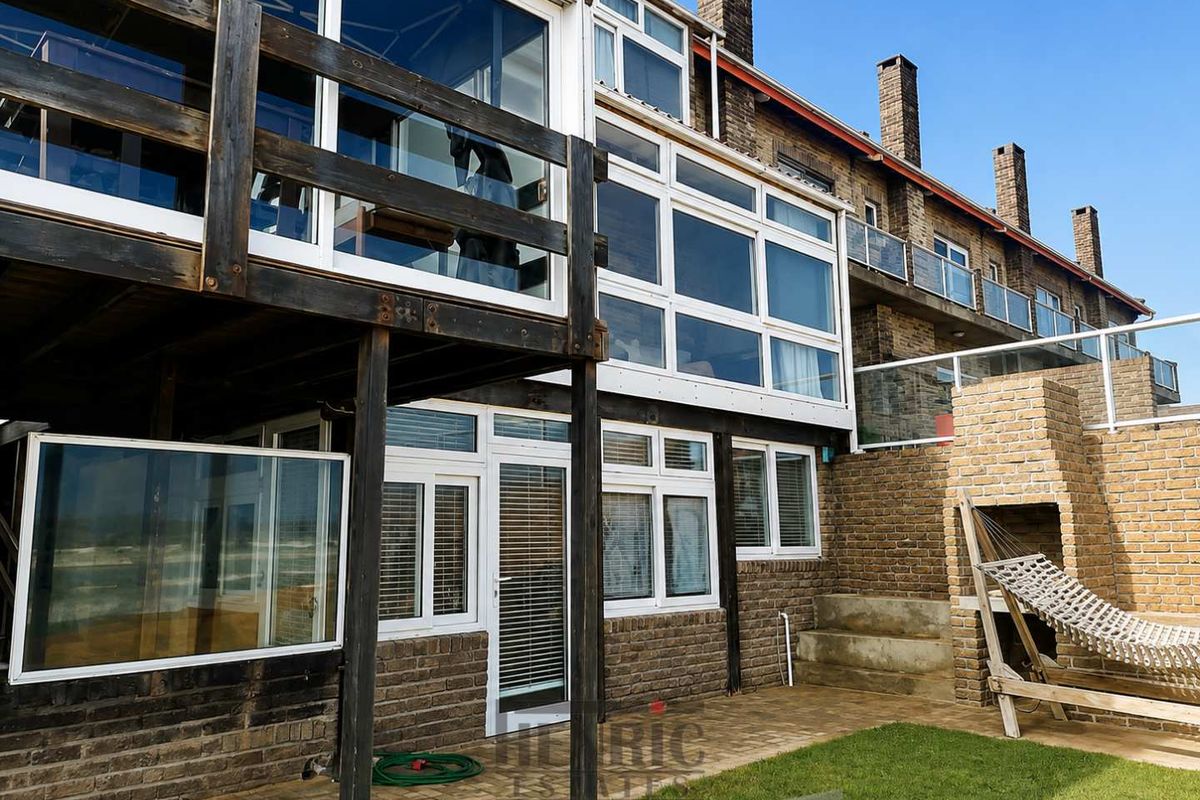 Rear exterior view of a multi-level townhouse featuring a timber balcony, brick facade, paved patio area, and a built-in outdoor brick fireplace.