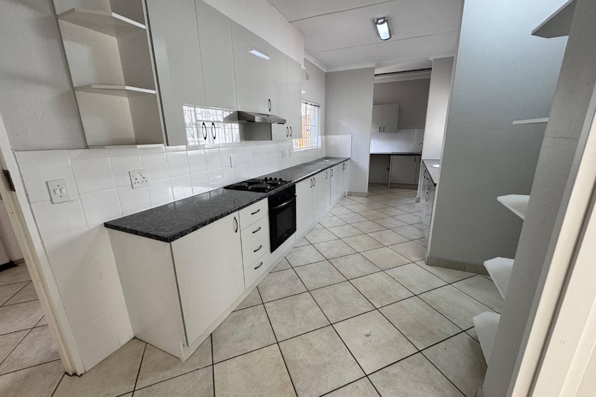 A functional kitchen featuring white cabinetry, dark laminate countertops, a built-in oven and hob, and tiled flooring, with an adjacent scullery area.
