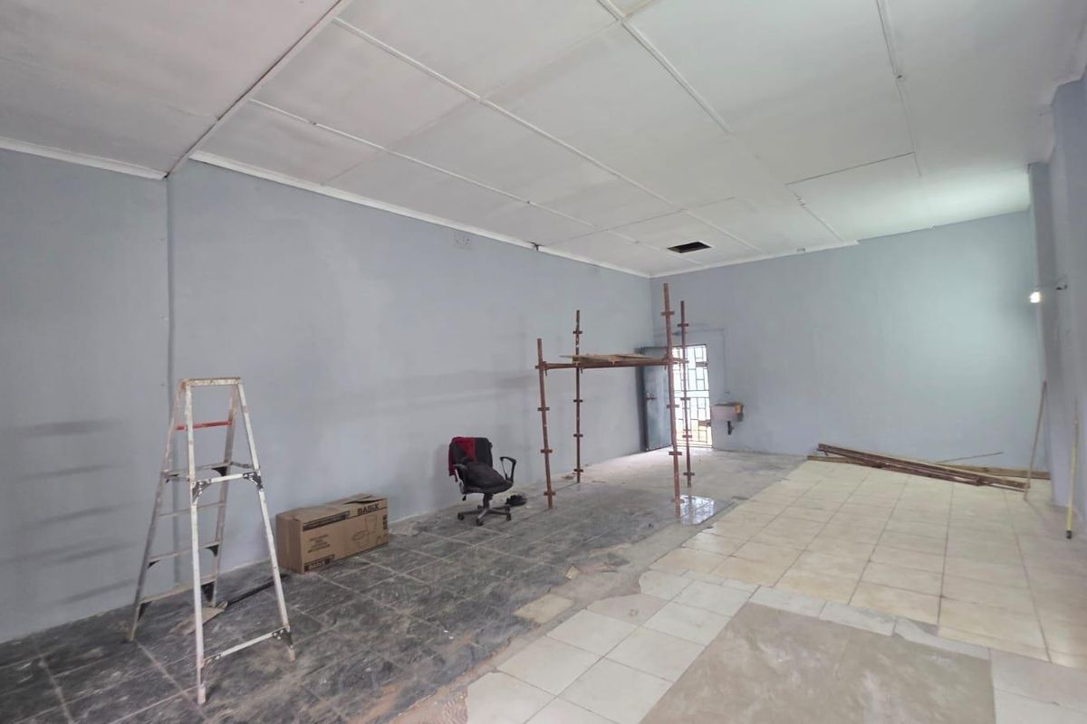 An open-plan commercial space currently undergoing renovations, featuring a suspended ceiling and mixed tiled flooring, suitable for various business configurations.