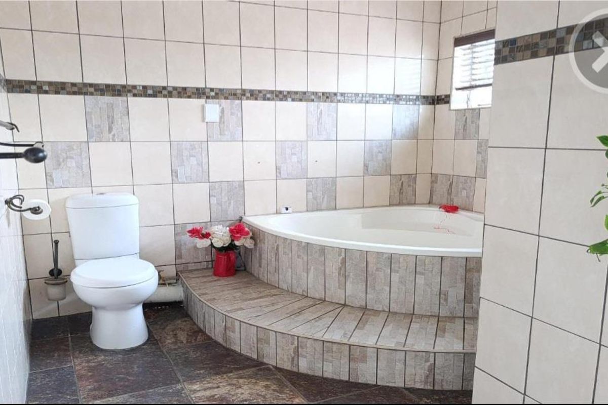 A bathroom featuring a raised corner bathtub with decorative stone-look tiling, a standard toilet, and neutral wall tiles with a mosaic accent border.