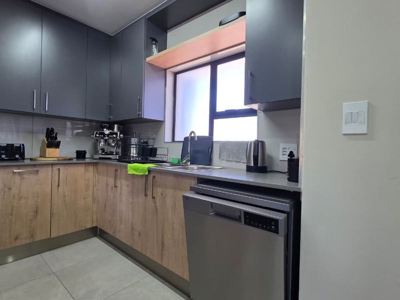 Modern kitchen featuring two-tone cabinetry, stone countertops, tiled flooring, and integrated dishwasher, offering a clean and functional workspace.