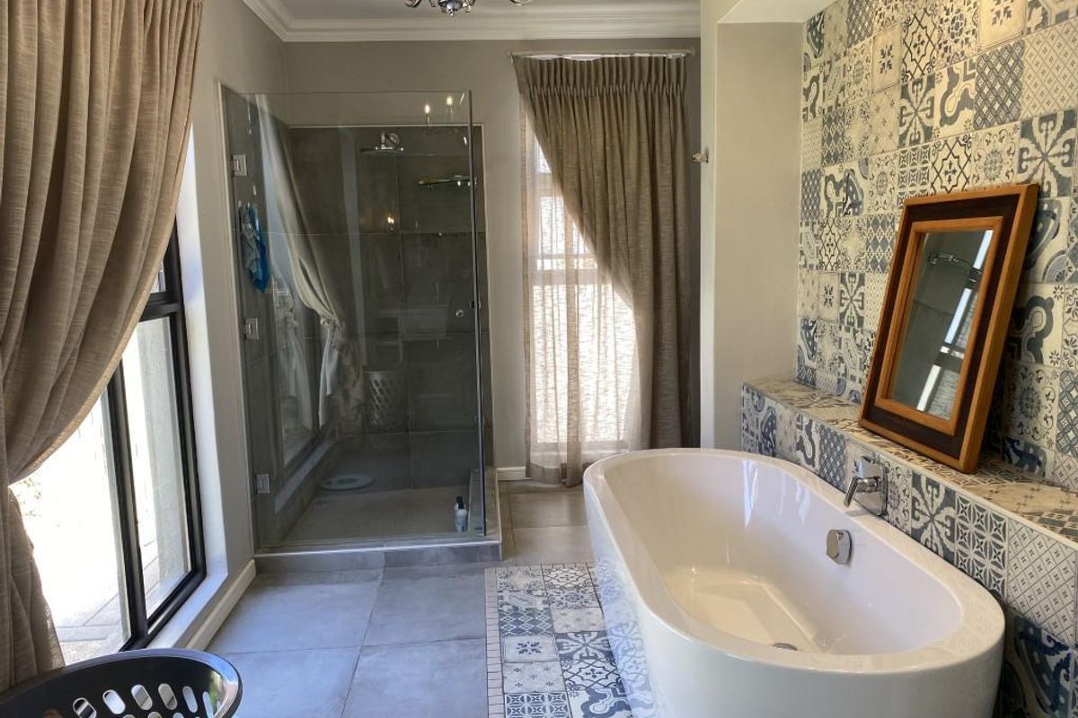 A modern bathroom featuring a freestanding bathtub, a glass-enclosed walk-in shower, and decorative patterned wall tiling.