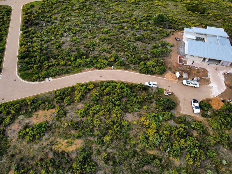 Aerial view of a residential property under construction, featuring a paved access road, driveway, and surrounding natural landscape.