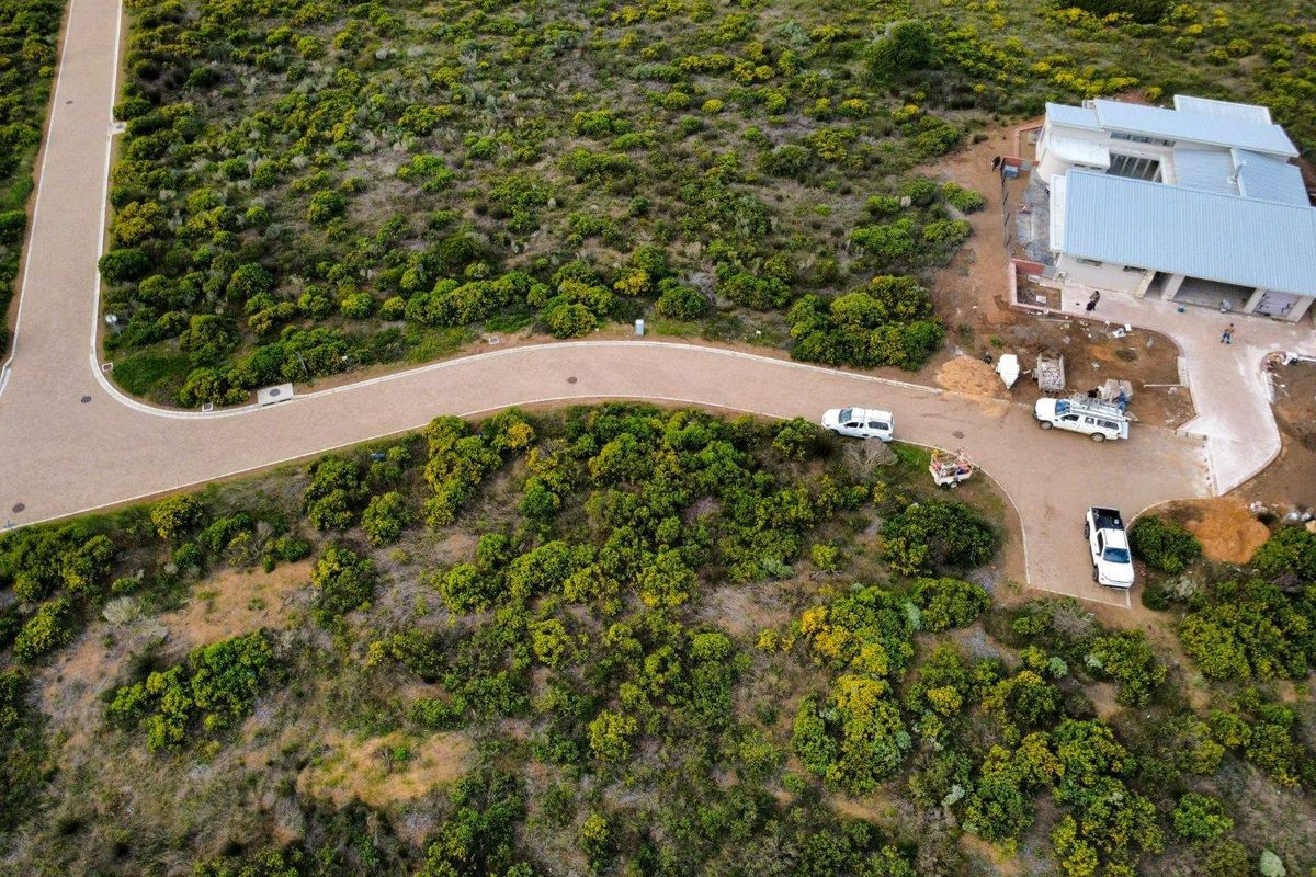 Aerial view of a residential property under construction, featuring a paved access road, driveway, and surrounding natural landscape.