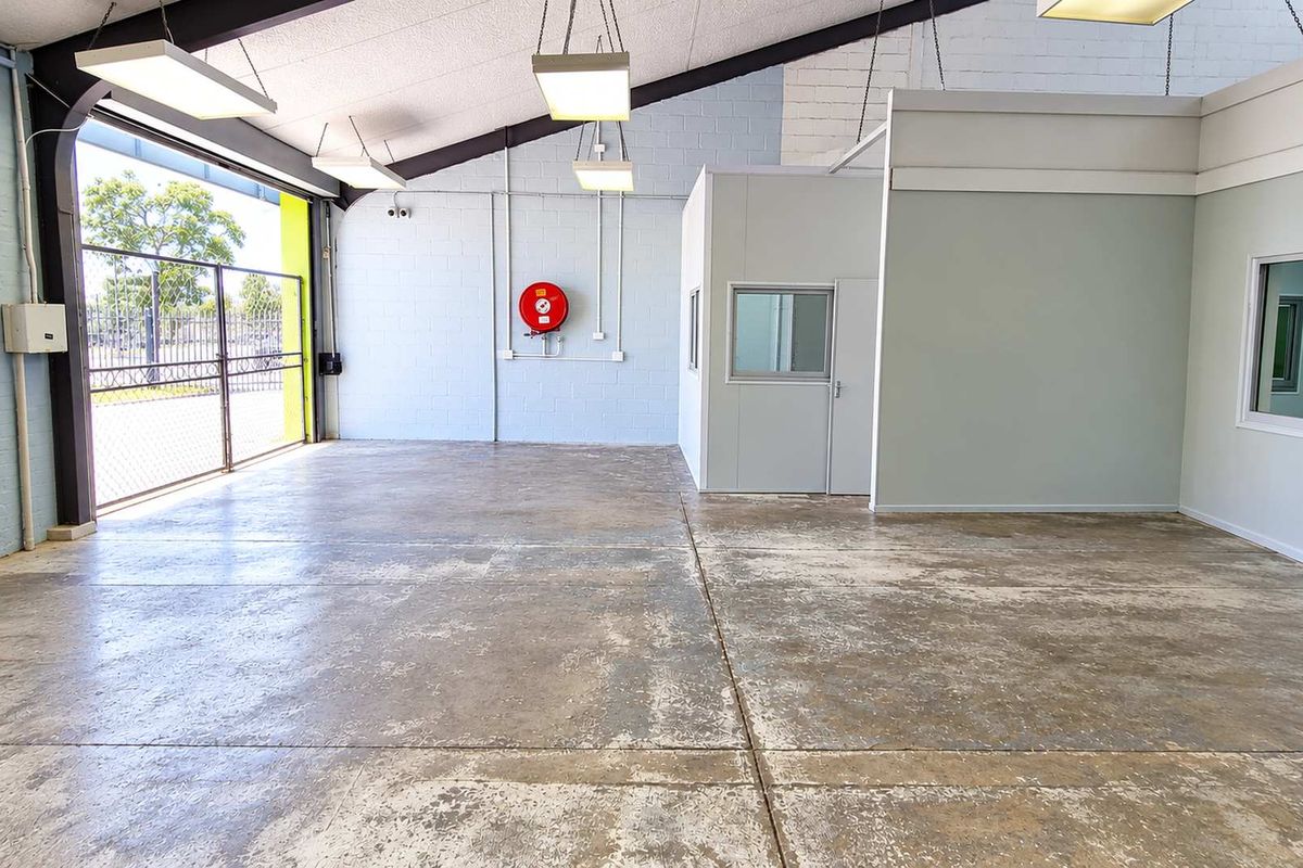 Spacious industrial utility area featuring concrete flooring, exposed steel beams, suspended lighting, and a partitioned office enclosure with a roller shutter door.