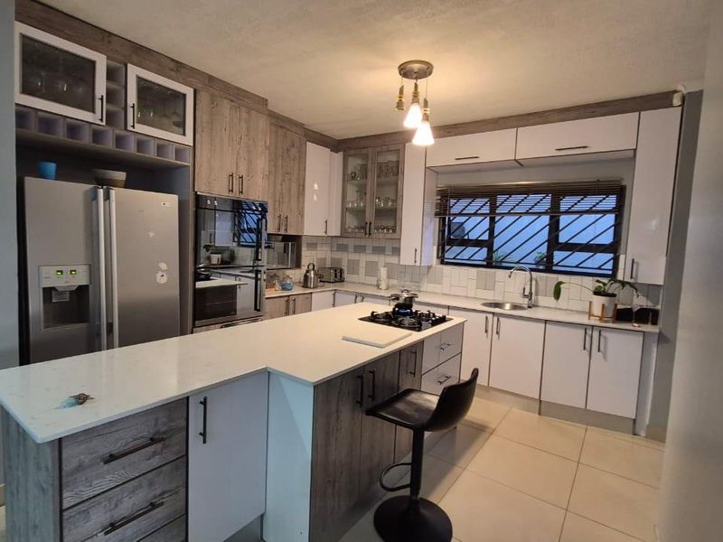 Modern kitchen featuring a central island with gas hob, stone countertops, ample built-in cabinetry, and tiled flooring.