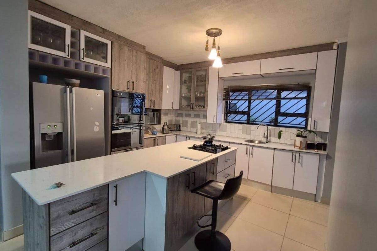 Modern kitchen featuring a central island with gas hob, stone countertops, ample built-in cabinetry, and tiled flooring.