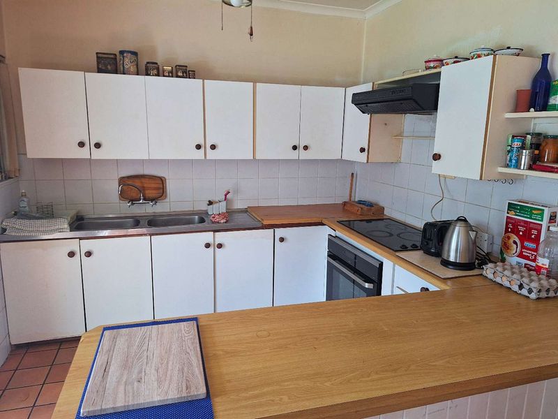 Functional kitchen featuring white cabinetry, laminate countertops, built-in oven, electric hob, and a double stainless steel sink with tiled backsplash.