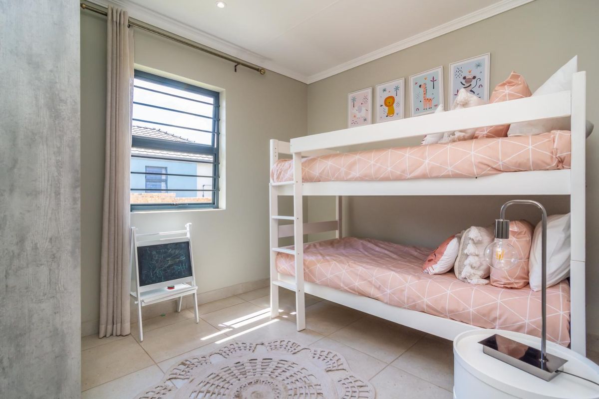 A bright and well-maintained bedroom featuring neutral wall tones, tiled flooring, and a window with security bars.