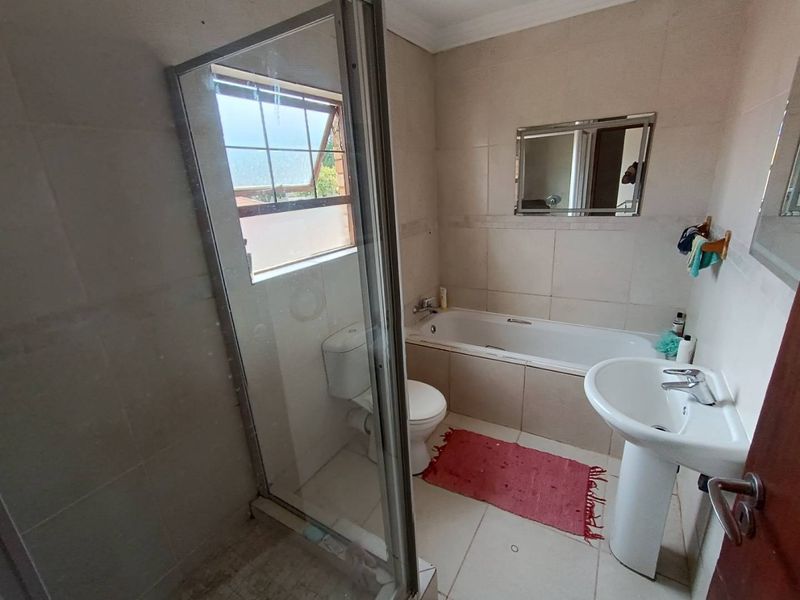 A functional bathroom featuring a shower enclosure, bathtub, pedestal basin, and toilet with neutral wall and floor tiling.