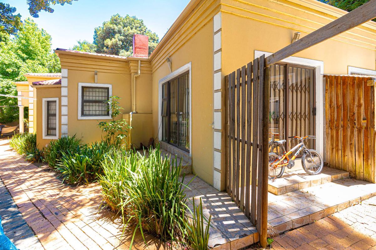 Rear exterior view of the house featuring a paved patio area, sliding glass doors with security gates, and established garden landscaping.