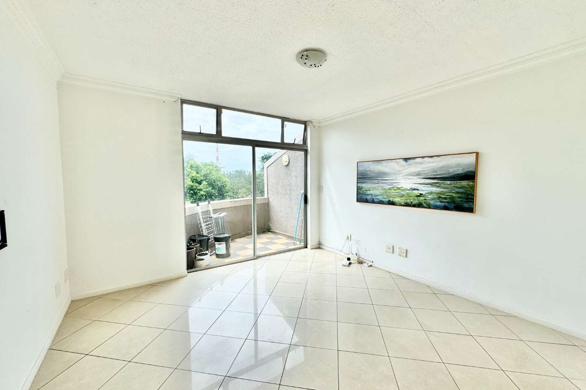A bright, open-plan living area featuring tiled flooring, a ceiling-mounted light fixture, and large sliding glass doors leading to a private balcony.