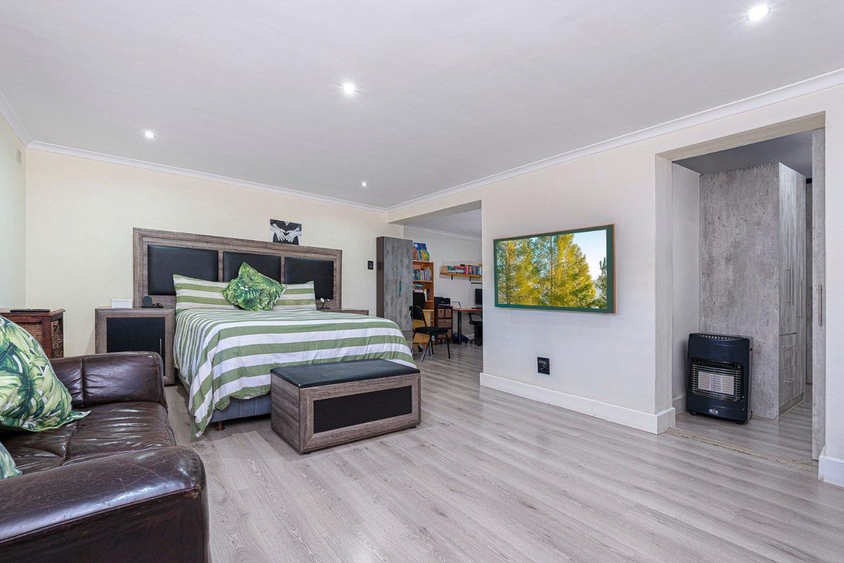 Spacious bedroom featuring light wood-look laminate flooring, recessed downlighting, and an adjoining study or dressing area.