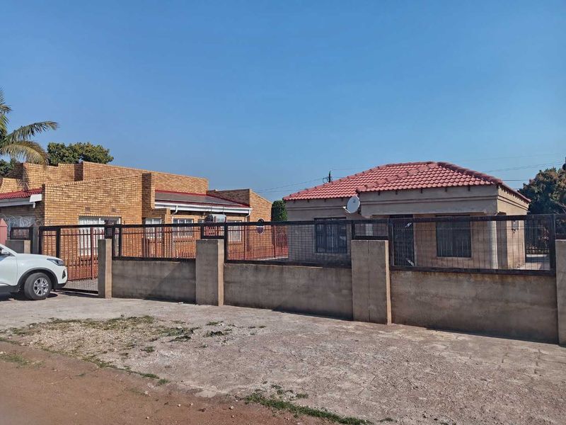 Front view of a residential property featuring face brick construction, a tiled roof, and a secure perimeter wall with metal fencing.