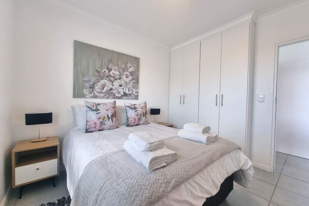 A bright and well-maintained bedroom featuring built-in floor-to-ceiling wardrobes and neutral tiled flooring.