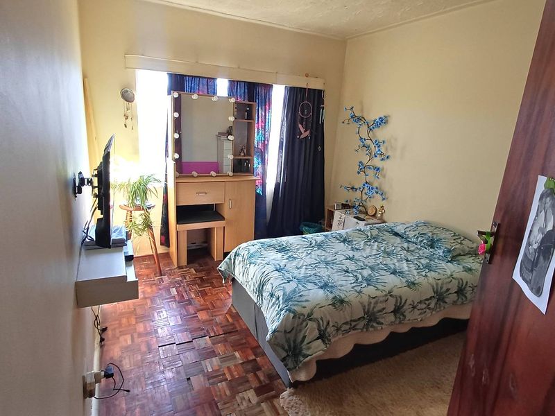 A bedroom featuring parquet flooring and a window, currently showing signs of wear on the floor and walls.