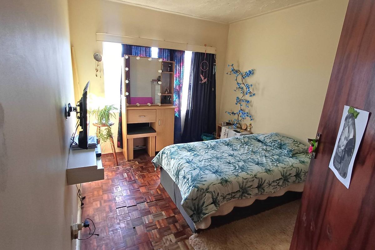 A bedroom featuring parquet flooring and a window, currently showing signs of wear on the floor and walls.