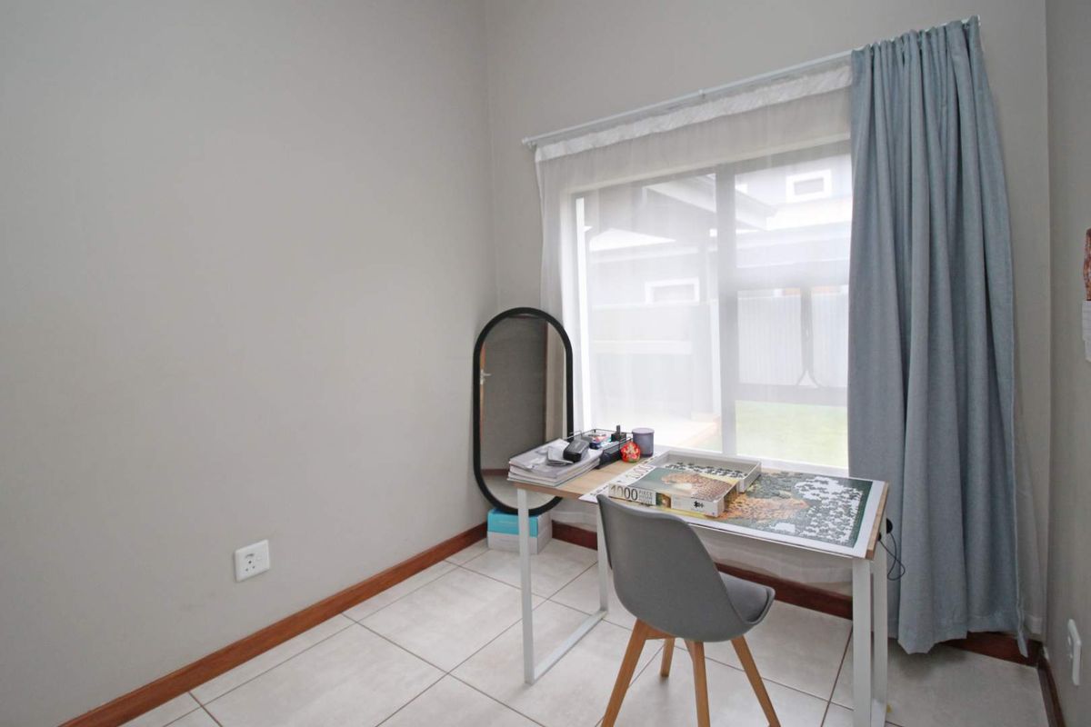 A functional bedroom space featuring neutral tiled flooring, a large window with curtain treatments, and standard electrical outlets.