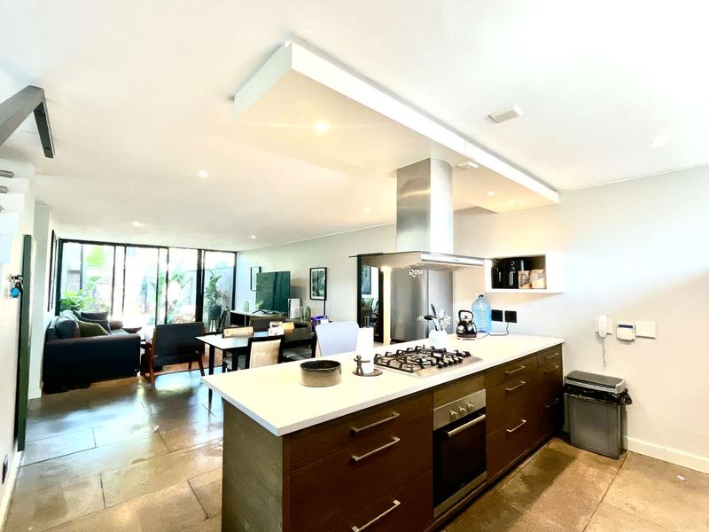 Modern open-plan living area featuring a central kitchen island with gas cooktop, stone countertops, and seamless flow to the outdoor patio through sliding glass doors.