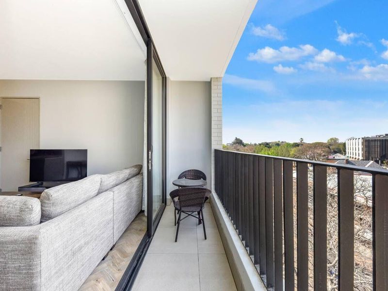 A modern apartment balcony featuring tiled flooring and a sleek metal balustrade, offering an open view of the surrounding neighborhood.