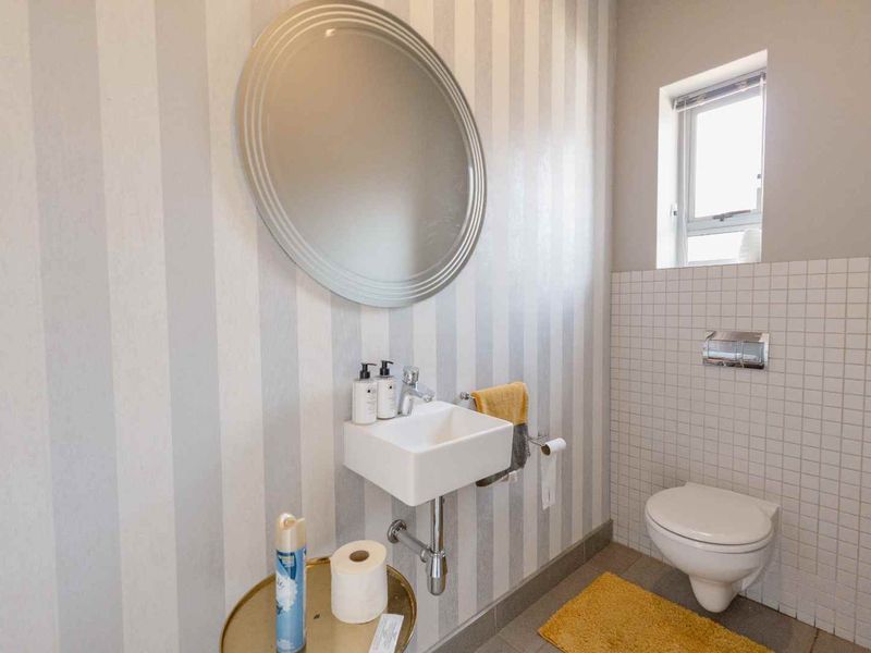 A compact guest bathroom featuring a wall-mounted basin, wall-hung toilet, and decorative striped wallpaper.