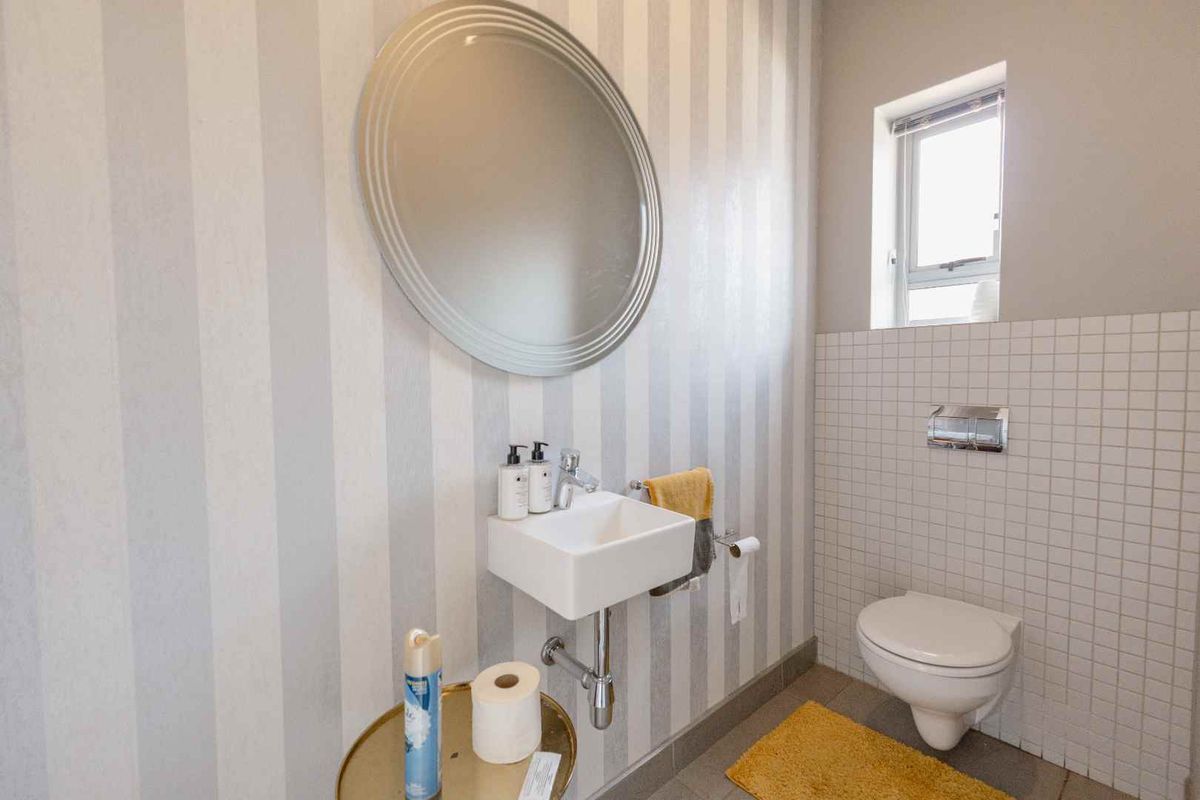 A compact guest bathroom featuring a wall-mounted basin, wall-hung toilet, and decorative striped wallpaper.