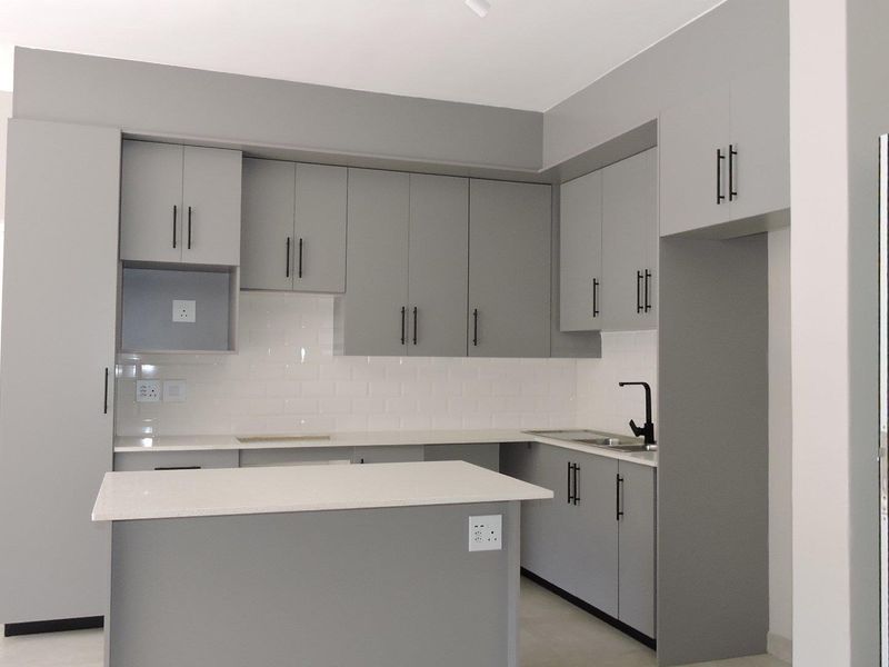 Modern kitchen featuring sleek grey cabinetry, stone countertops, a subway tile backsplash, and a functional island, presenting a clean and contemporary aesthetic.